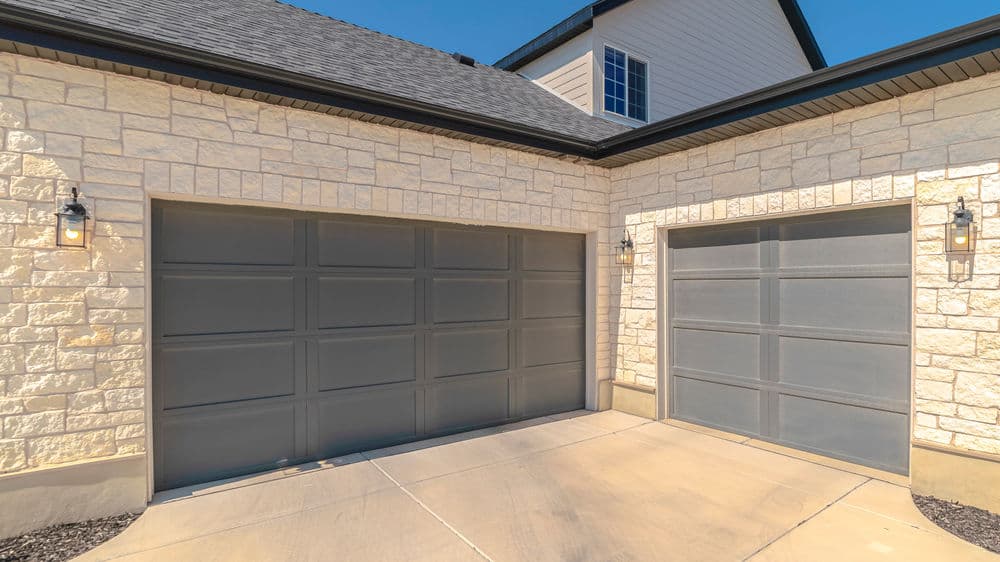 Modern home exterior featuring two gray garage doors and stone facade. Bright sunny day.