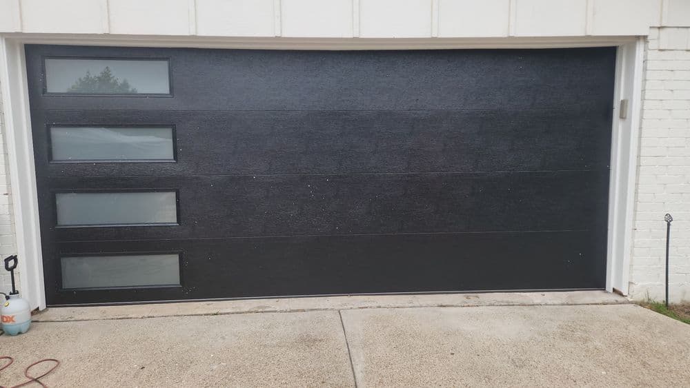 Modern black garage door with horizontal panels and glass windows. Stylish curb appeal enhancement.