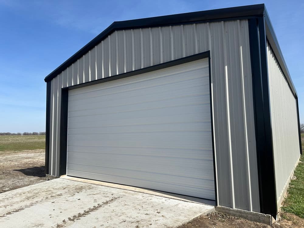 Metal storage building with a large roll-up door against a clear blue sky.