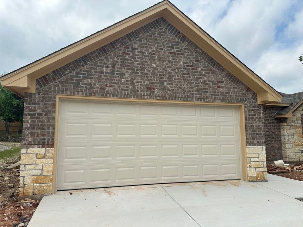 Newly constructed home with a brick exterior and beige garage door under a cloudy sky.