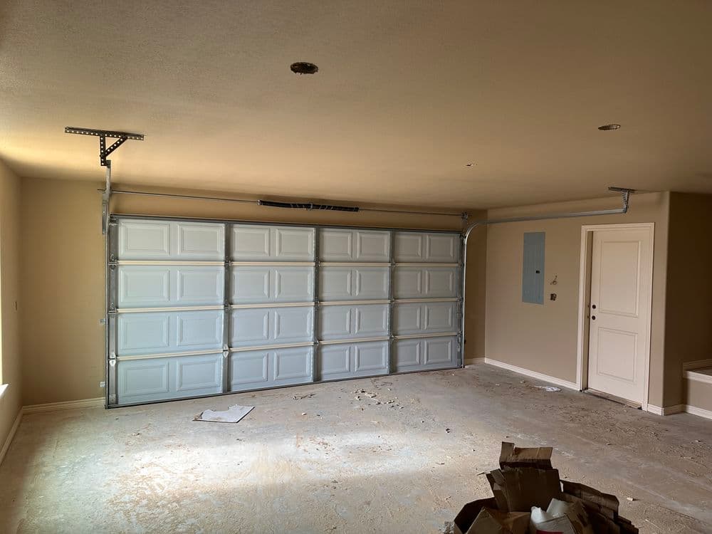 Newly built garage interior with a white garage door, bare walls, and construction debris.