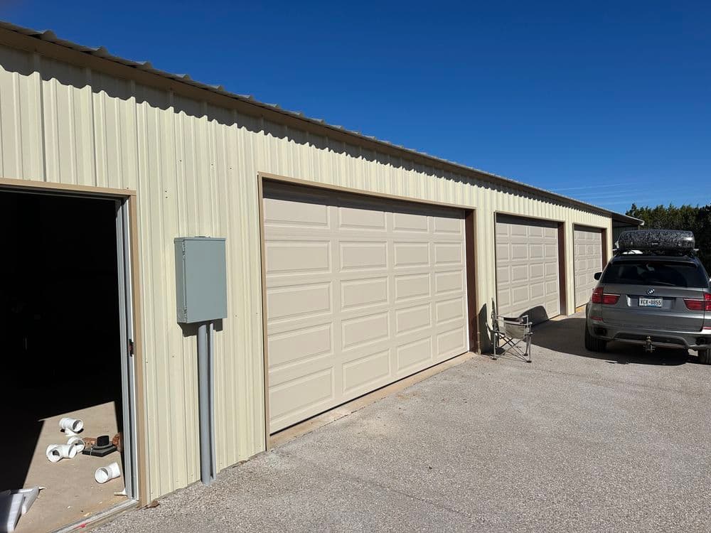 Metal storage building with three garage doors and a parked car on a sunny day.