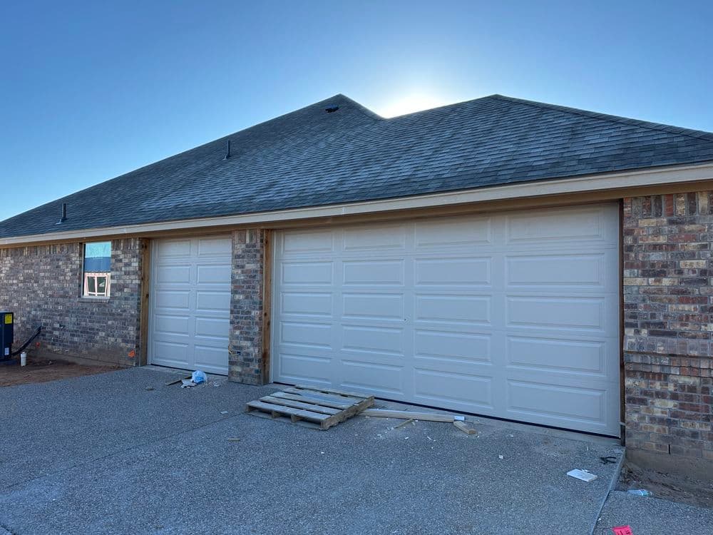 Two white garage doors on a brick home with a blue sky in the background.