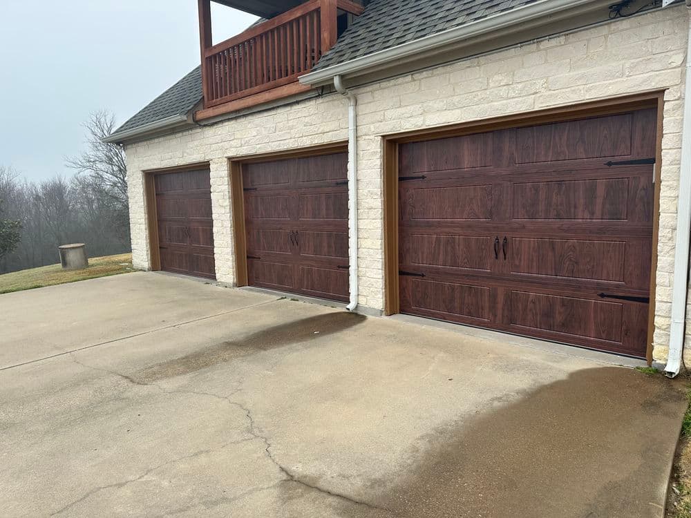 Modern home with three wooden garage doors on a stone exterior and concrete driveway.