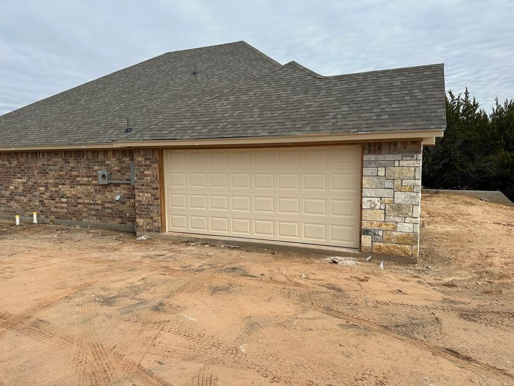 Newly constructed home featuring a beige garage door and brick facade on a dirt lot.