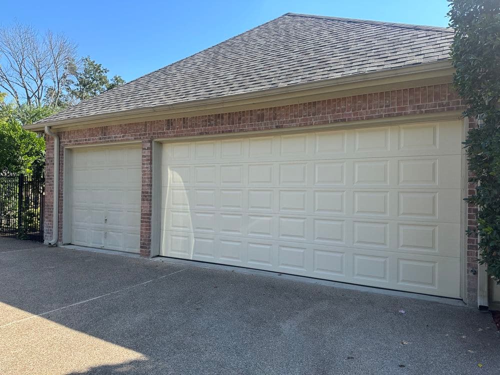 Two closed garage doors in a residential brick home with a clear blue sky.