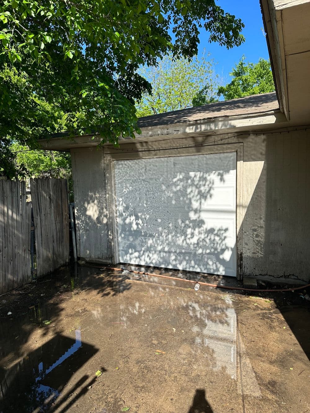 Garage with closed door and water puddles reflecting trees under a clear blue sky.