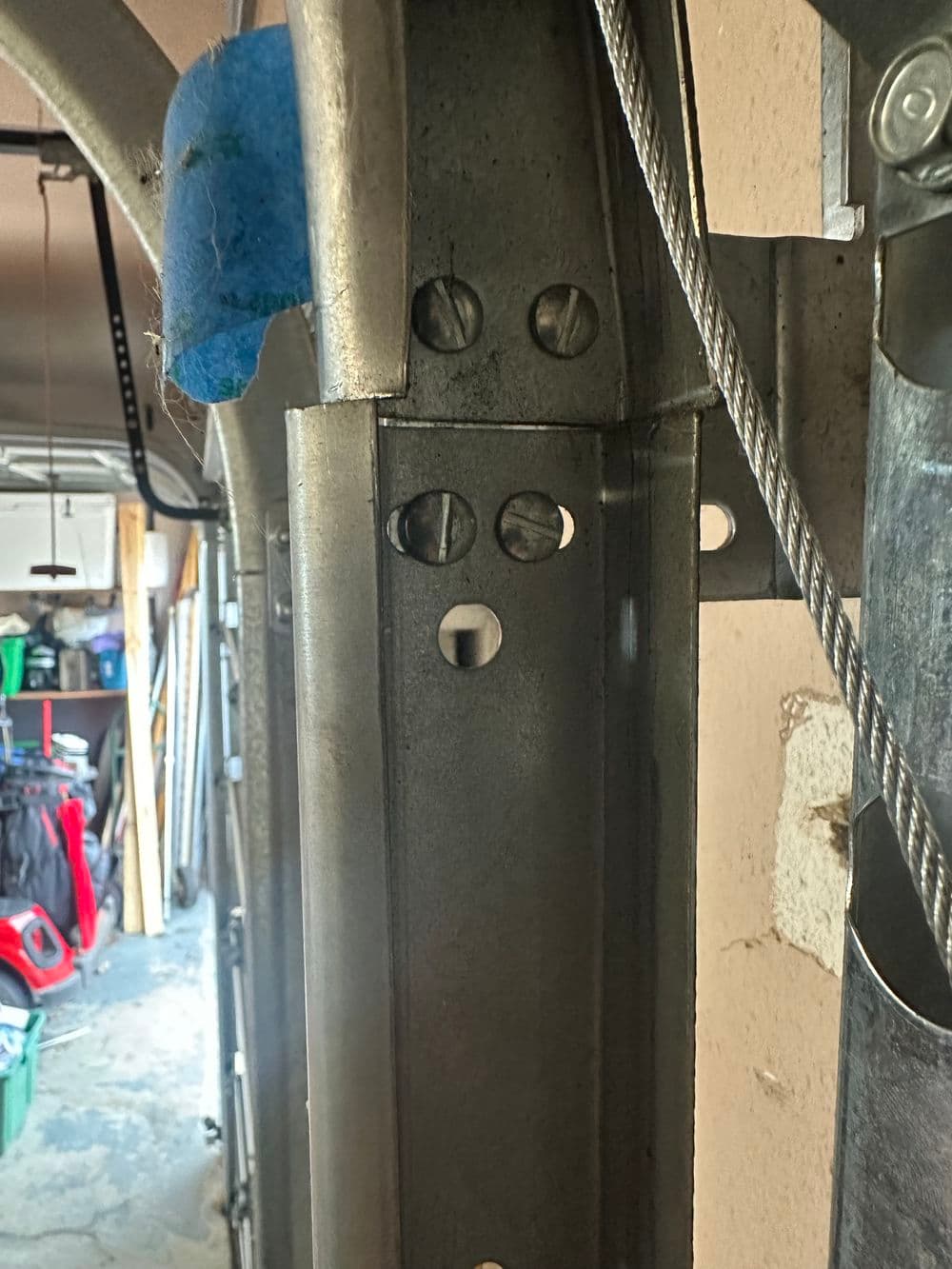 Close-up of metal frame with holes, wires, and blue material in garage setting.