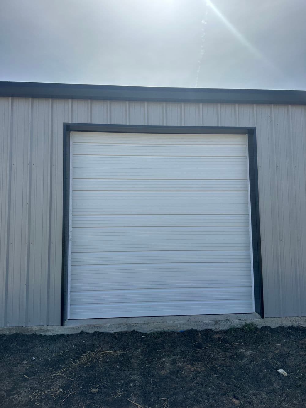 White roll-up garage door on a metal building with a clear sky above.