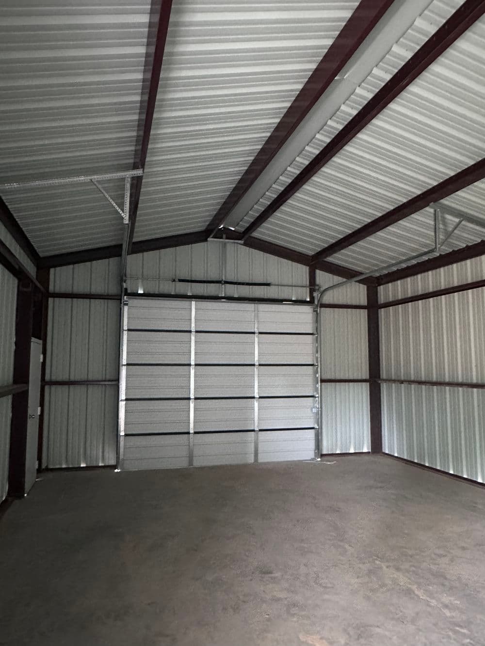Interior of a spacious metal storage shed with high ceilings and large roll-up door.