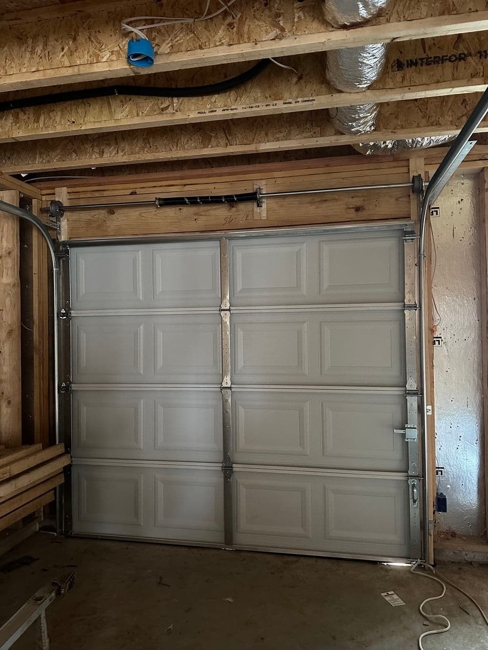 Interior view of a garage with a closed gray overhead door, exposed beams, and ductwork.