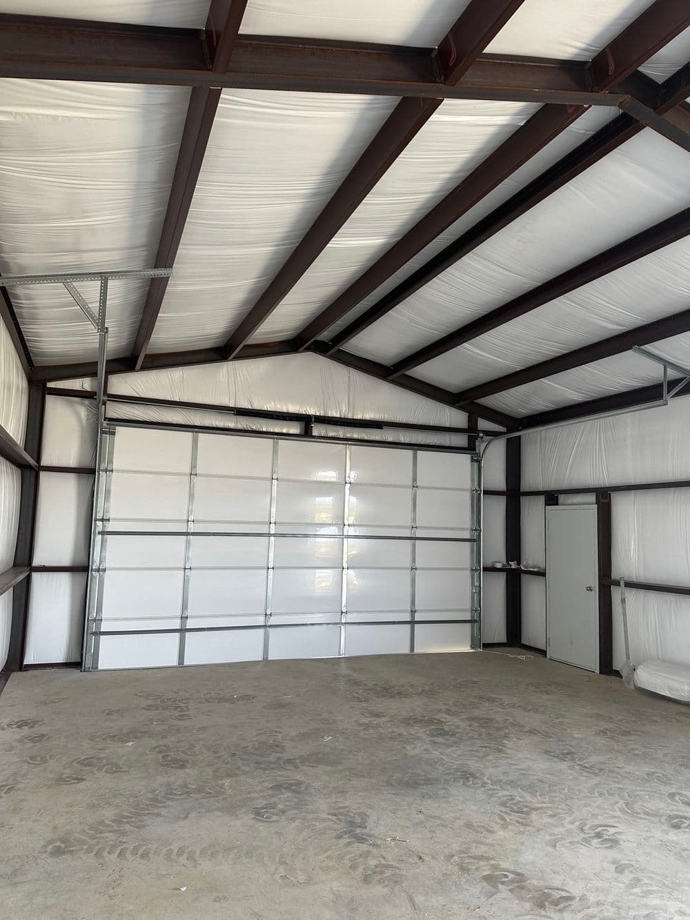 Interior of a spacious, insulated metal garage with a large roll-up door and concrete floor.
