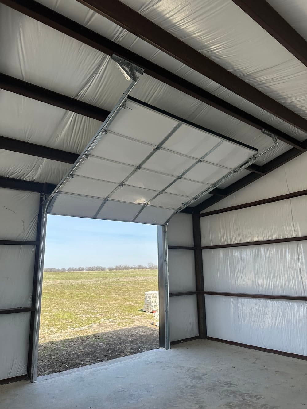 Interior of a metal building with an open garage door revealing a grassy landscape outside.