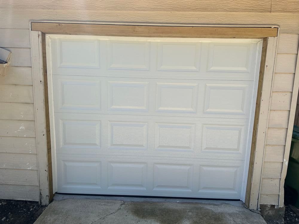 White garage door with panel design, newly installed and framed against beige wall.