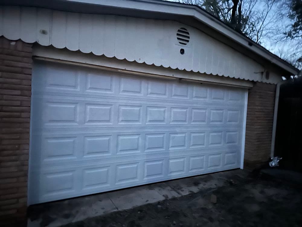 White garage door on a brick home exterior at dusk with trees in the background.