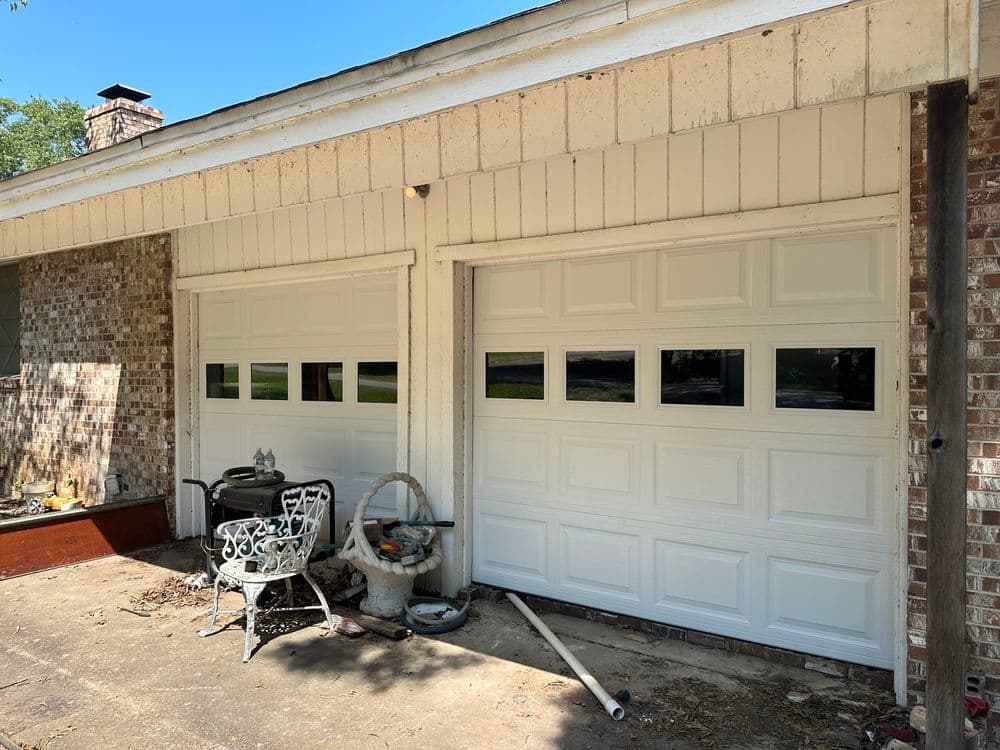 White garage doors with windows beside a patio set in a residential setting.