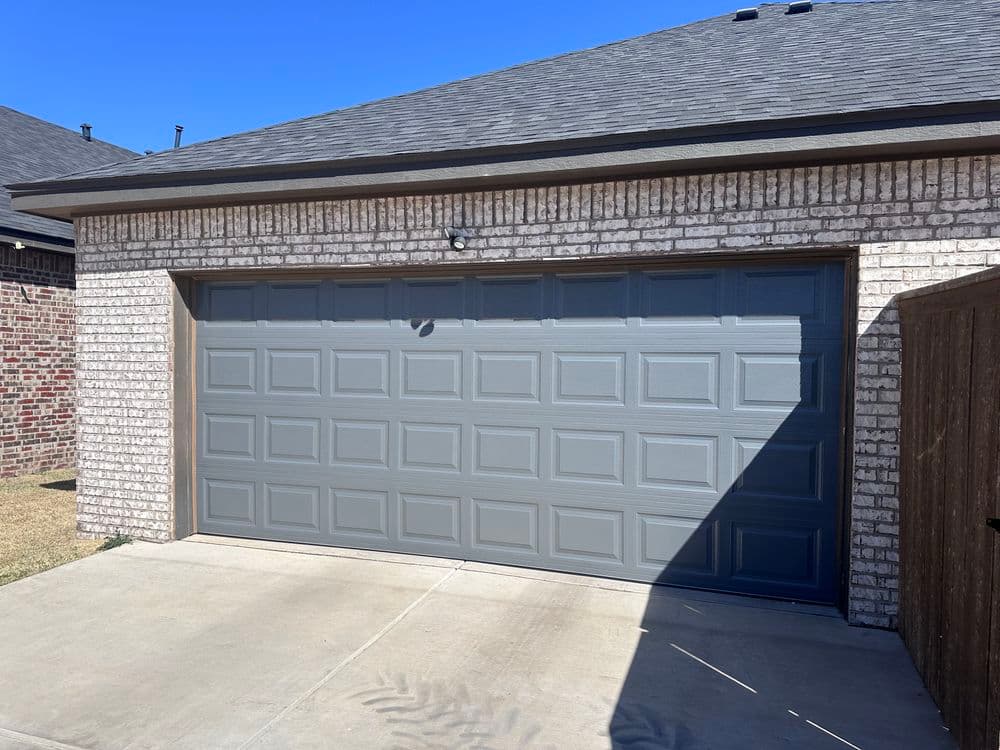 Modern garage door on a brick house with a clear blue sky. Well-maintained driveway.