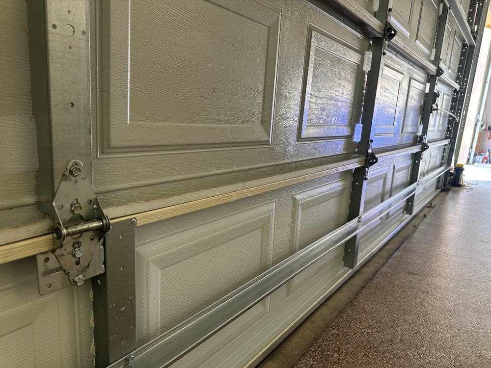 Close-up of a garage door track and panel, showcasing metal hardware and textured surface.