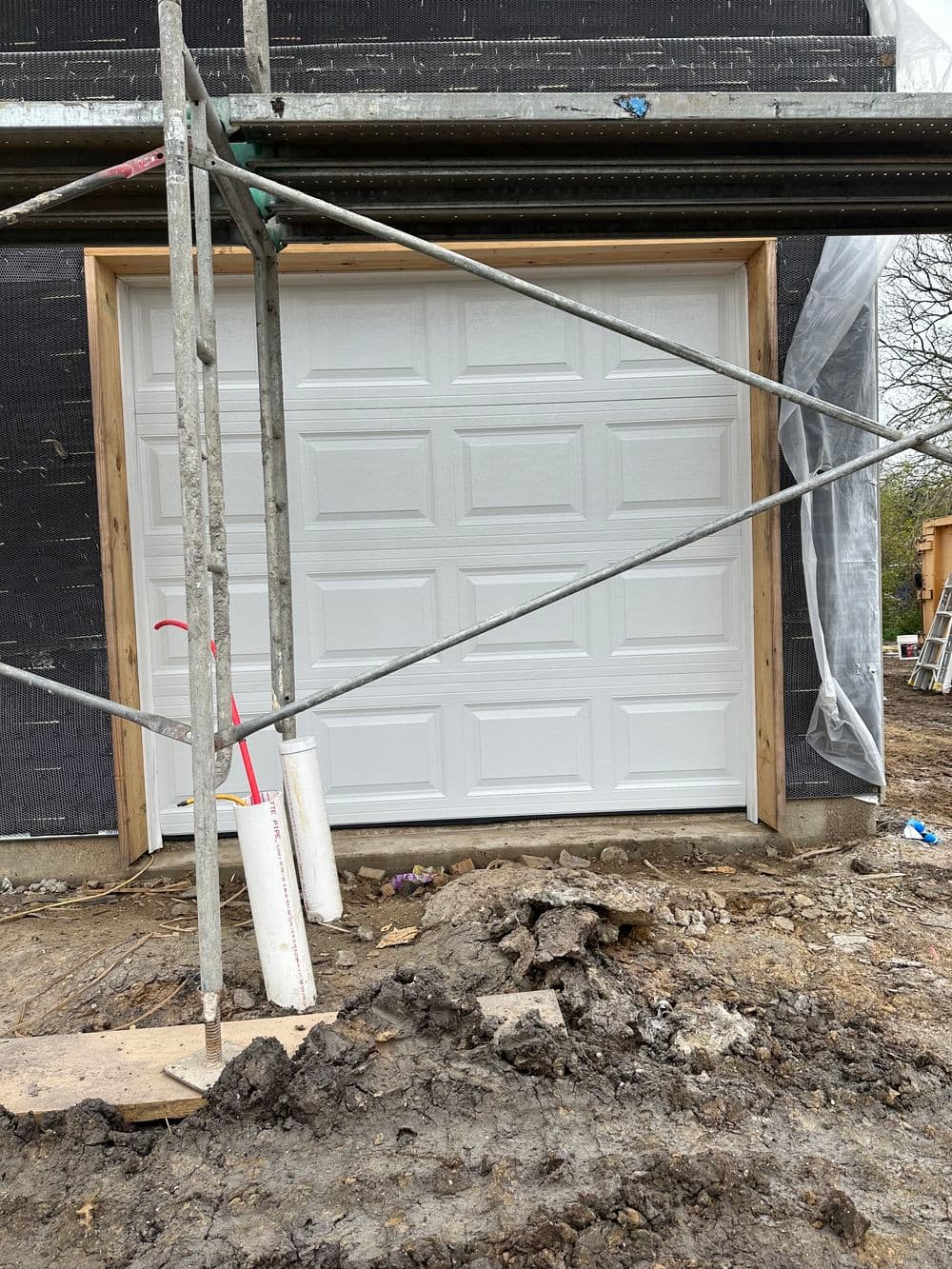 Newly installed white garage door framed with wooden structure at a construction site.