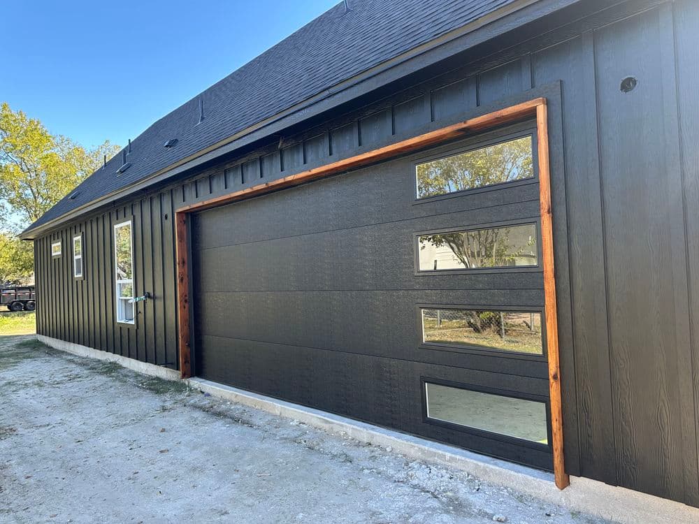 Modern black garage with large windows and wooden trim, set against a blue sky.