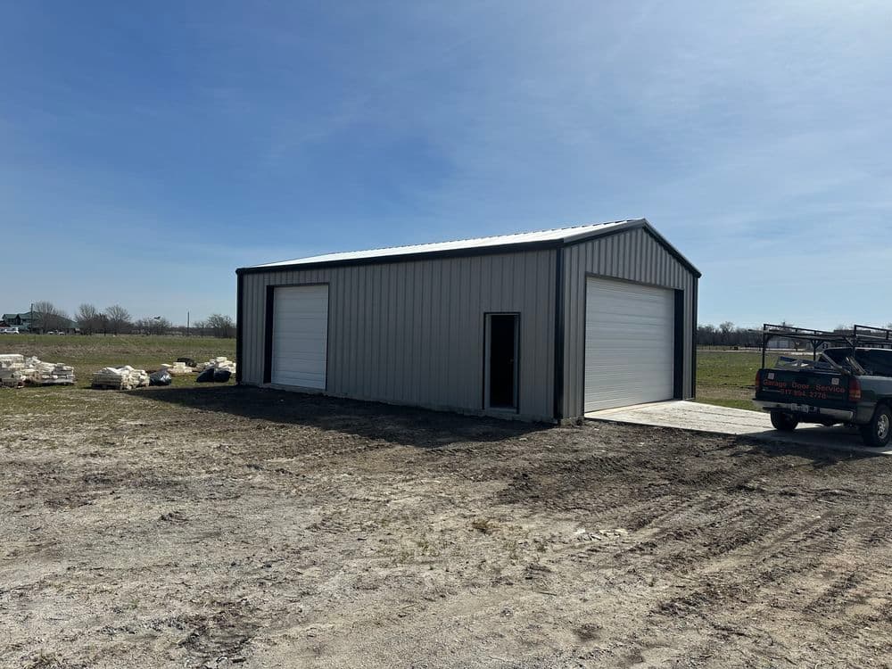 Metal storage building with two large doors and gravel driveway in open field.