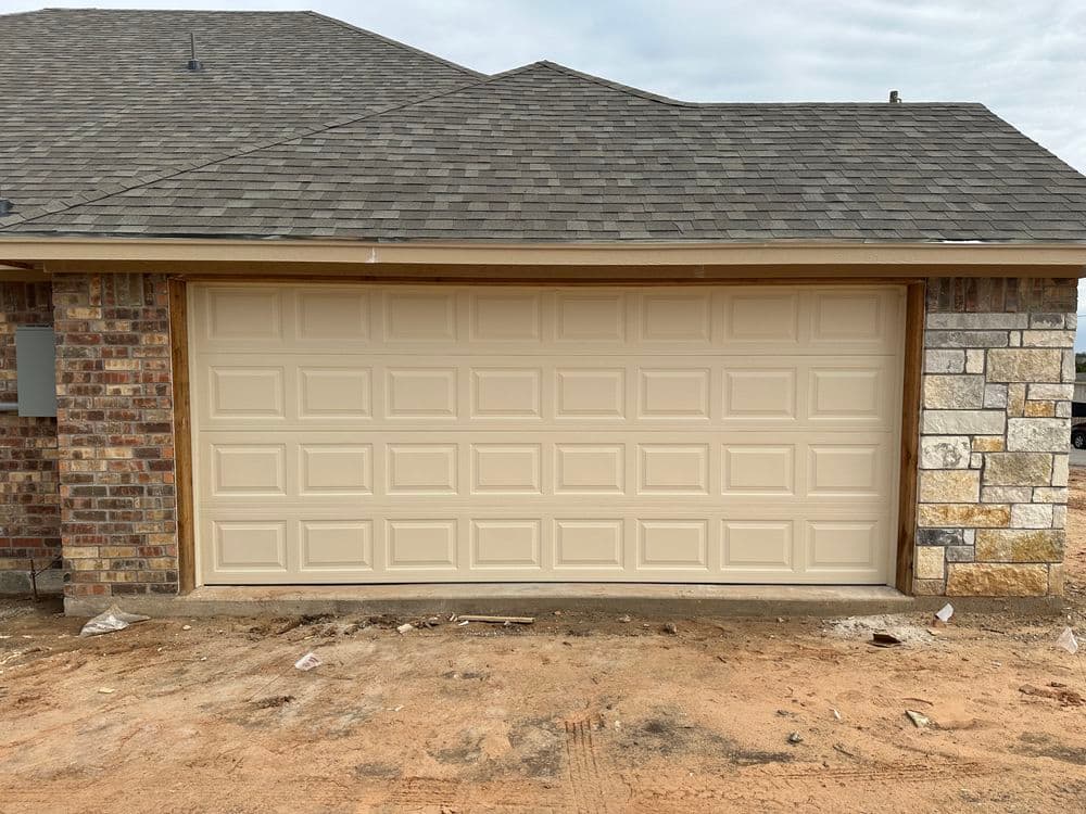 New beige garage door on a brick and stone house with a gray roof.