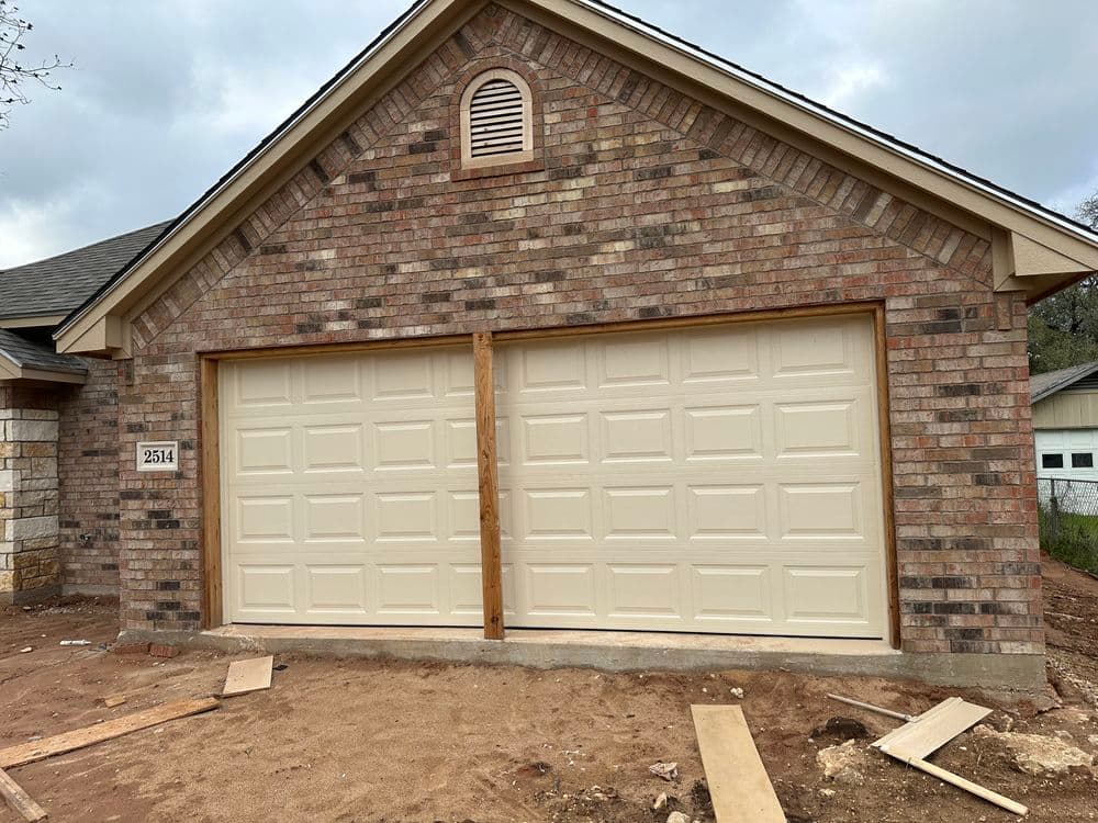 Newly built brick house with two-car garage doors, under construction, and wooden framing visible.
