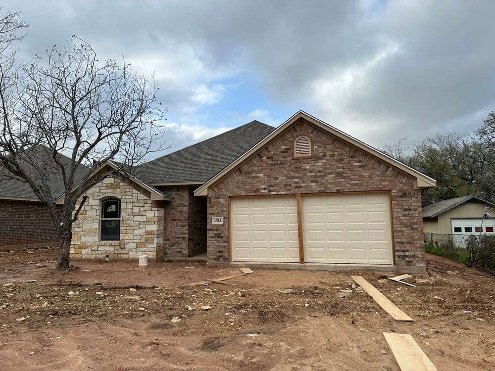 Newly constructed brick home with a two-car garage and unfinished landscaping.